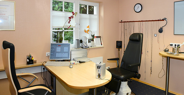 Modernes Arztpraxis-Behandlungszimmer mit Schreibtisch, Computer und Untersuchungsstuhl.